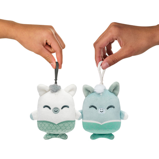 Two hands holding Plushiverse Happy Hippocampus Plushmates Besties keychains, one white and one teal, both designed to look like smiling fantasy creatures with mermaid tails from the TeeTurtle Myths & Cryptids collection.