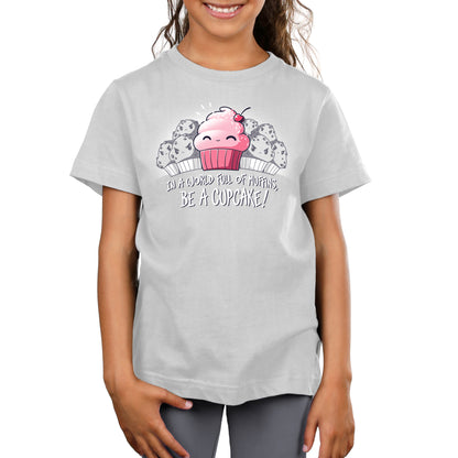 A girl wearing a white "Be a Cupcake" t-shirt from TeeTurtle with a pink cupcake on it.
