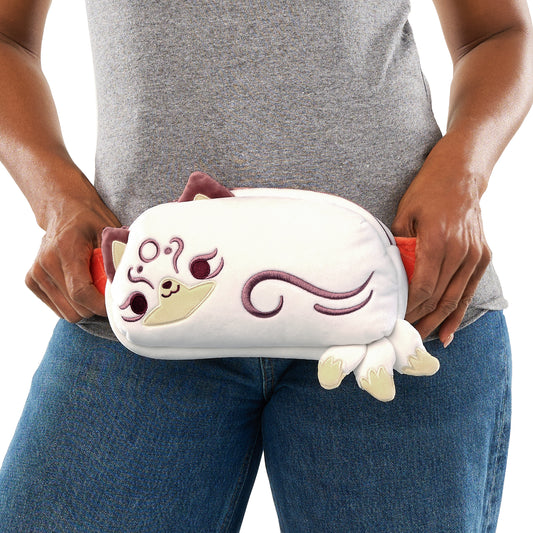 A person in a gray t-shirt and blue jeans holding a Plushiverse Magical Kitsune Fanny Pack from TeeTurtle, shaped like a white cat with purple details.