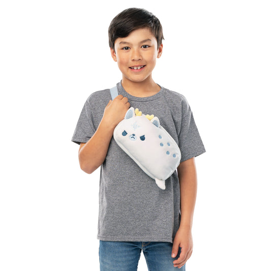A young boy smiling at the camera, holding a TeeTurtle Plushiverse White Stag Fanny Pack in the shape of a unicorn over his shoulder.