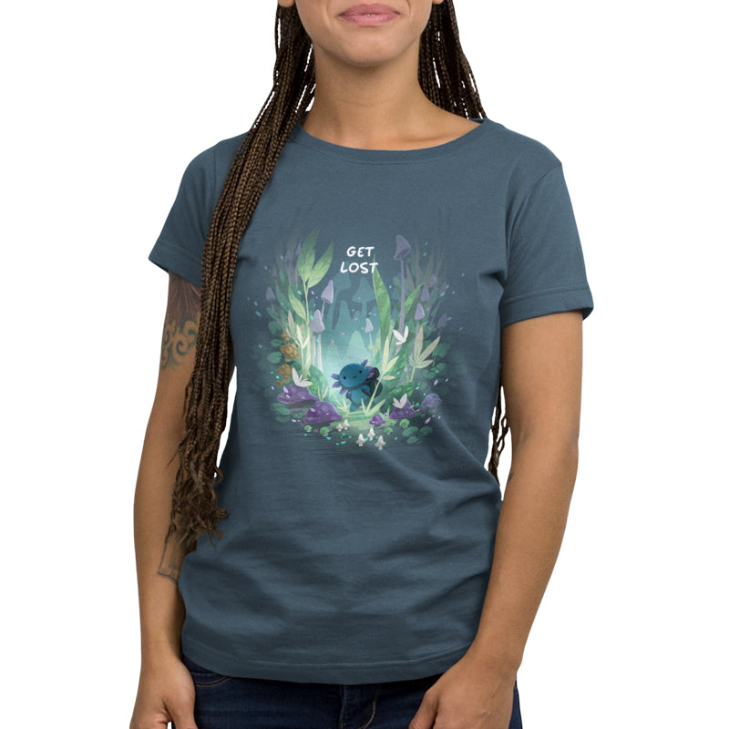 A woman wearing a Monster Digital Axolotl Explorer denim blue unisex tee with a "get lost" forest-themed graphic design, standing against a plain background.