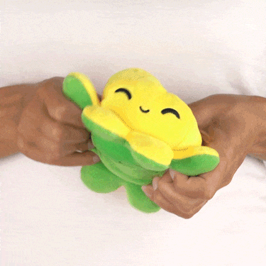 Two hands squeezing a smiling yellow and green TeeTurtle Reversible Octopus Plushie (Lemon + Lime) toy, which appears to be a flower or sun character.