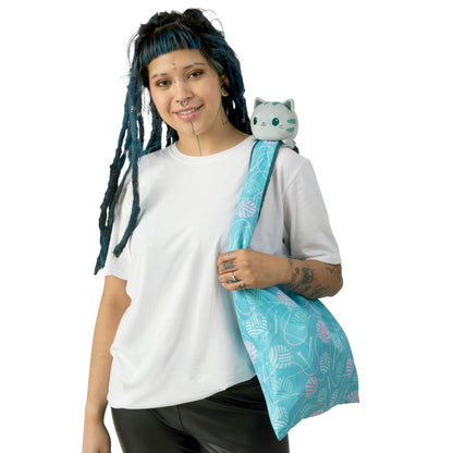 A woman holding a blue Plushiverse Crafty Cat Plushie Tote Bag with a TeeTurtle logo on it.