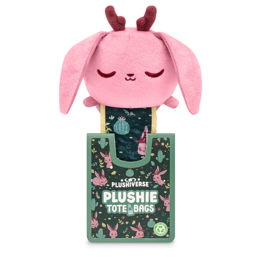 A Plushiverse Fearsome Jackalope plushie tote bag with pink ears and a serene expression, protruding from a decorative green box labeled 