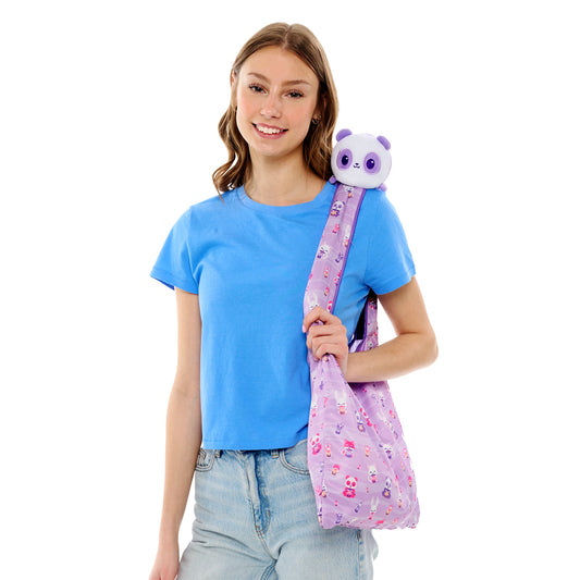 Young woman smiling with a Plushiverse Bobalicious Panda plushie from TeeTurtle on her shoulder and carrying a matching tote bag.