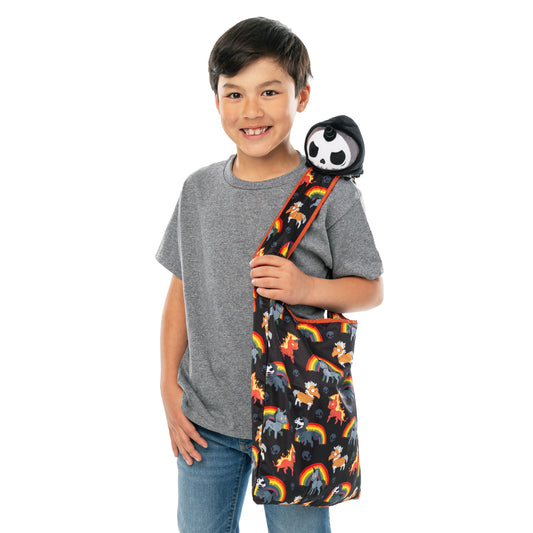 Young boy smiling at the camera, wearing a gray t-shirt and denim jeans, holding a colorful TeeTurtle Plushiverse Unicorns of the Apocalypse Plushie Tote Bag with a panda design over his shoulder.