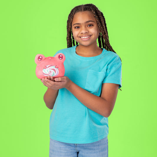 A young girl holding a TeeTurtle Plushiverse Lollihop Frog 4” Reversible Plushie on a green background.