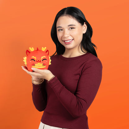 A woman holding a TeeTurtle Plushiverse Lunar New Year Dragon 4" Reversible Plushie on an orange background.