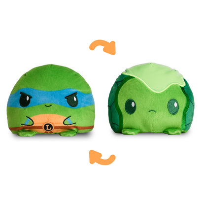 A reversible green plushie featuring Leonardo from the Teenage Mutant Ninja Turtles on one side and a baby turtle covered in ooze on the other. 