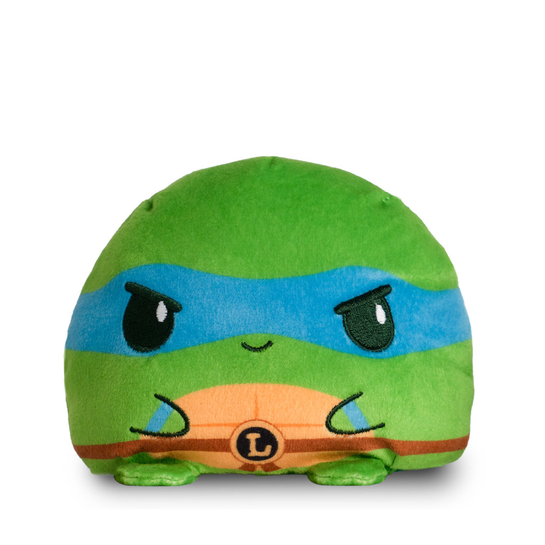A reversible green plushie featuring Leonardo from the Teenage Mutant Ninja Turtles on one side and a baby turtle covered in ooze on the other. 