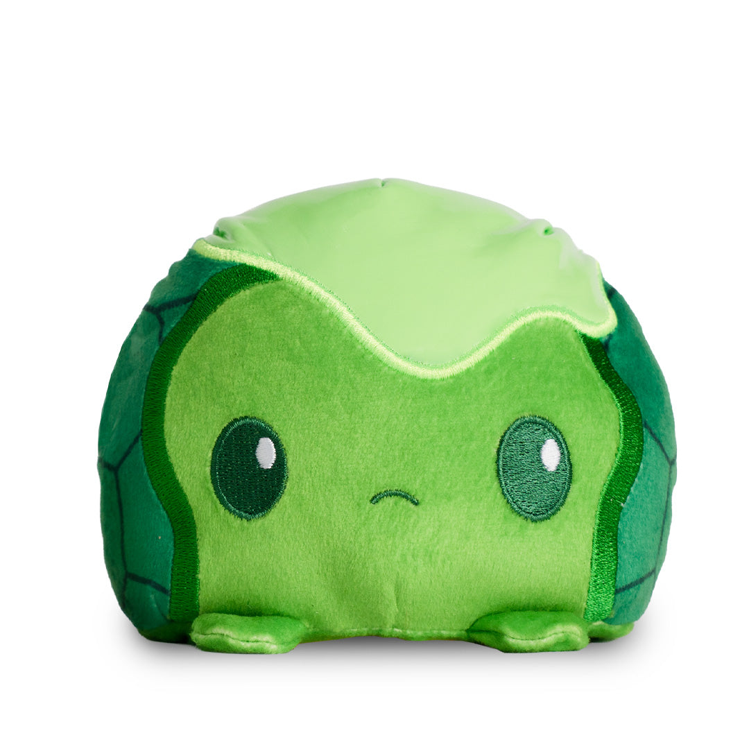 A reversible green plushie featuring Leonardo from the Teenage Mutant Ninja Turtles on one side and a baby turtle covered in ooze on the other. 