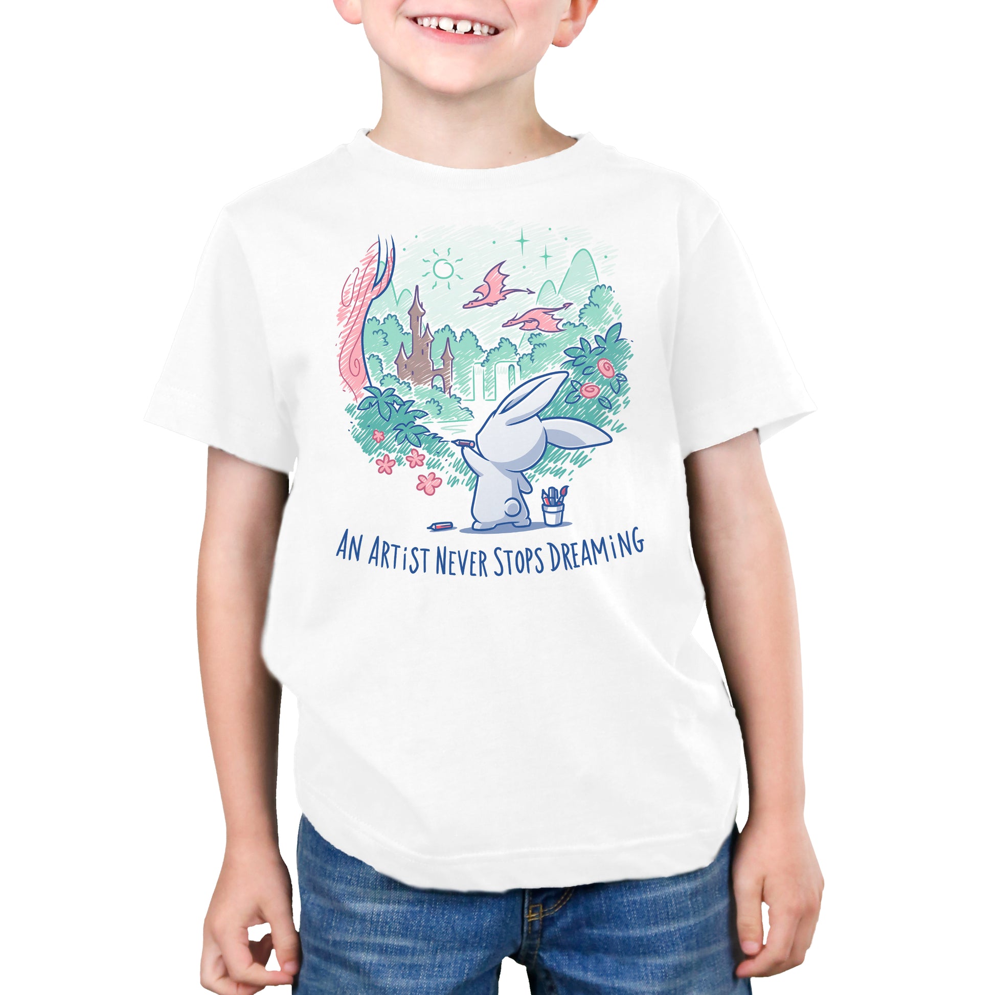 A young boy wearing a white t-shirt from TeeTurtle showcasing his creativity with the winter-themed design "An Artist Never Stops Dreaming".