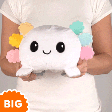 A woman is holding up a TeeTurtle Big Reversible Axolotl Plushie (Rainbow Gills) that says big.