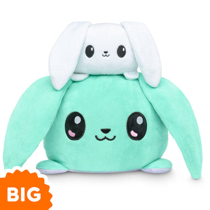 A green bunny and a white bunny, both TeeTurtle Big Reversible Bunny Plushies (Light Purple + Aqua), sitting on top of each other.