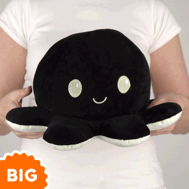 A woman is holding a black TeeTurtle Big Reversible Octopus Plushie (Green Glow + Black).