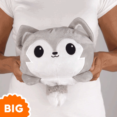 A woman is holding a TeeTurtle Big Reversible Wolf Plushie (Light Gray), which perfectly matches her mood.