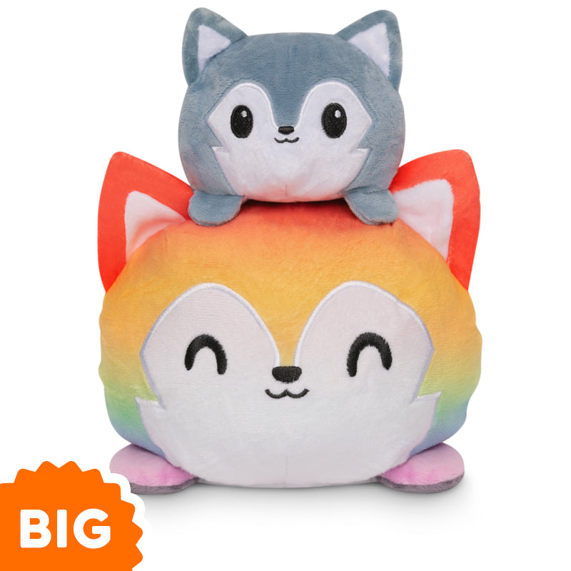 A TeeTurtle Big Reversible Wolf Plushie (Rainbow + Dark Gray) is stacked on top of another stuffed animal.