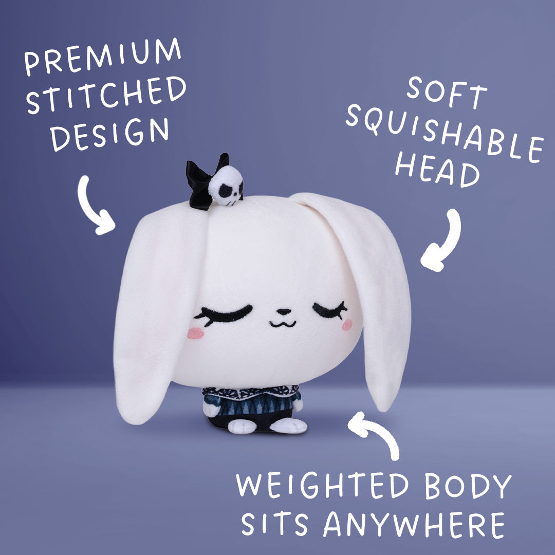 A white plush bunny toy with long floppy ears, a small black-and-white skull accessory on its head, and a weighted body, shown on a blue-gray background with white text callouts reading 'PREMIUM STITCHED DESIGN,' 'SOFT SQUISHABLE HEAD,' and 'WEIGHTED BODY SITS ANYWHERE.'.