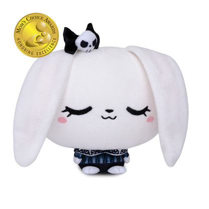 A white plush bunny character with long floppy ears, closed embroidered eyes, pink cheeks, and a small black-and-white skull accessory on its head. The plush is wearing a dark patterned skirt and standing against a plain white background.