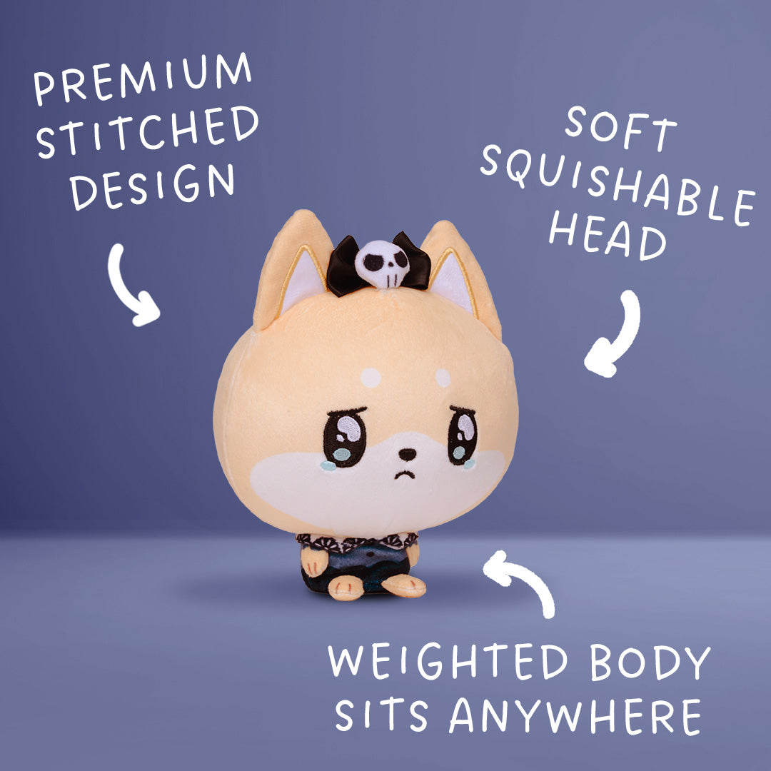 A cute chibi-style plush dog toy with a sad face, wearing a small black and white skull headband and black outfit, shown on a blue-gray background with white text callouts highlighting features like premium stitched design, soft squishable head, and weighted body that sits anywhere.