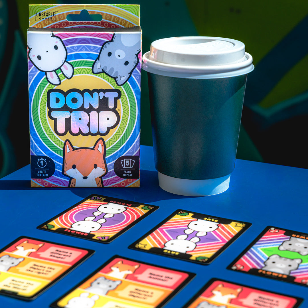 The "Don't Trip" base game by Unstable Games features cartoon animals on the box all staring at the viewer, with psychedellic rainbow cocentric circles behind them and the game title in the center. "Don't Trip" is a fast-paced party game that puts players' attention to detail to the test.