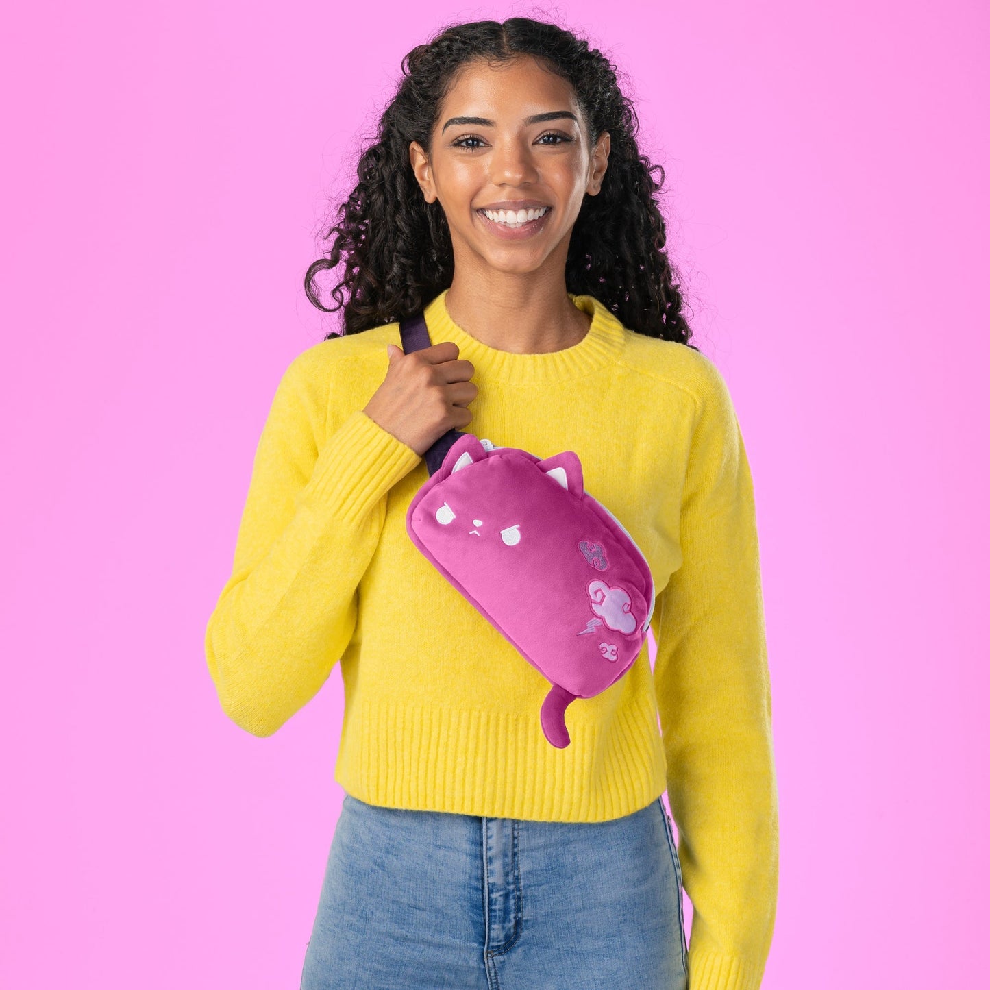 A woman wearing a yellow sweater and a TeeTurtle Plushiverse Thunder Paws Plushie Fanny Pack with an adjustable belt, perfect for festivals.