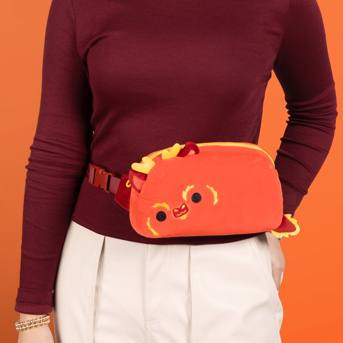 A woman enjoying hands-free functionality with an adorable Plushiverse Lunar New Year Dragon Plushie Fanny Pack by TeeTurtle featuring a cat design and an adjustable belt.