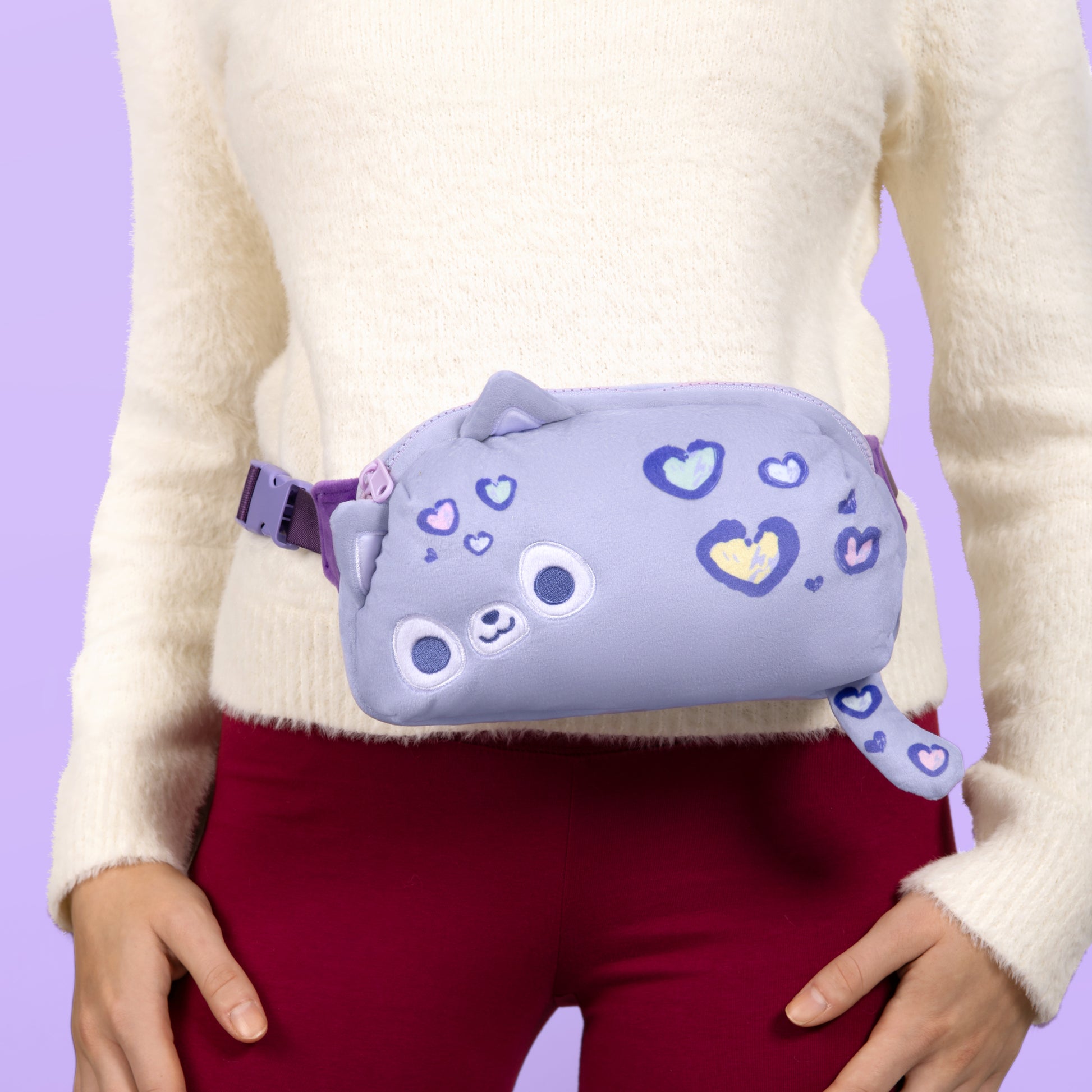 A woman sporting a trendy TeeTurtle Plushiverse A Spot in My Heart Leopard Plushie Fanny Pack, complete with heart patterns, offering hands-free functionality and an adjustable belt.