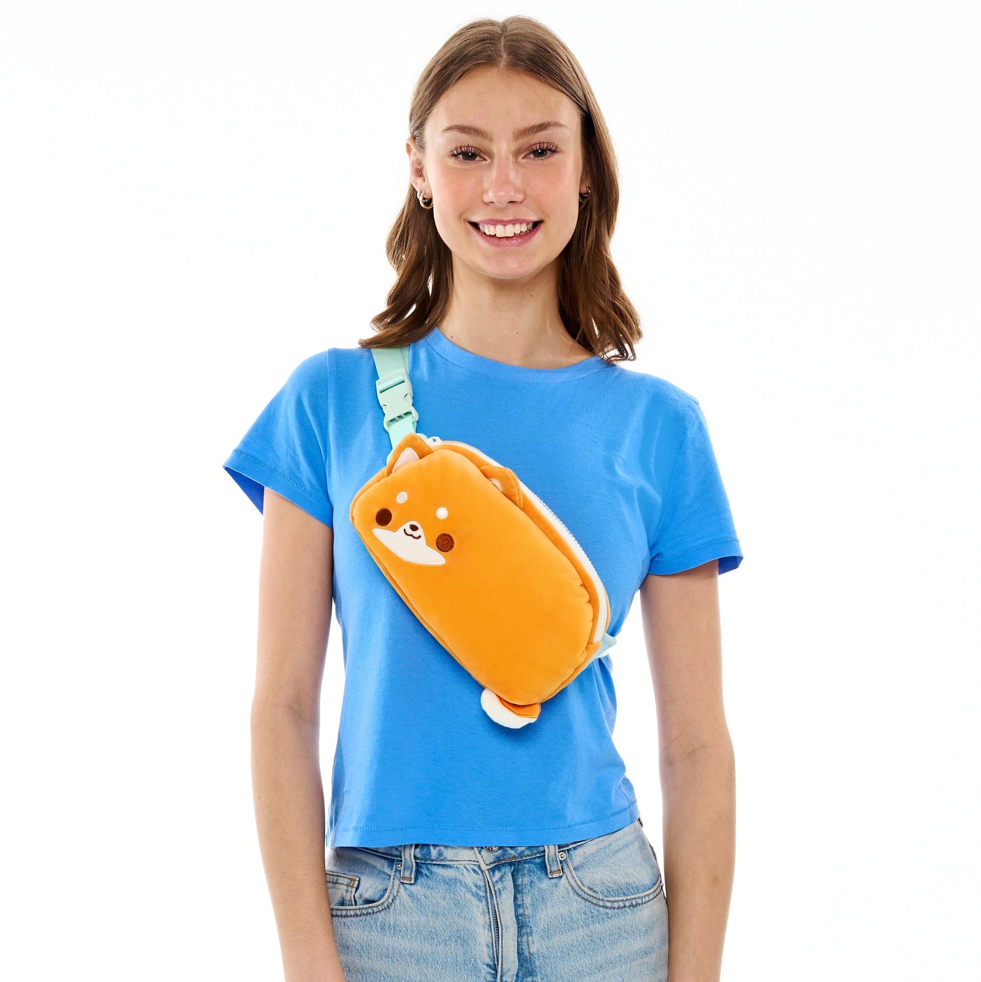 Woman in a blue t-shirt smiling with a TeeTurtle Plushiverse Super Shiba Plushie Fanny Pack over her shoulder.