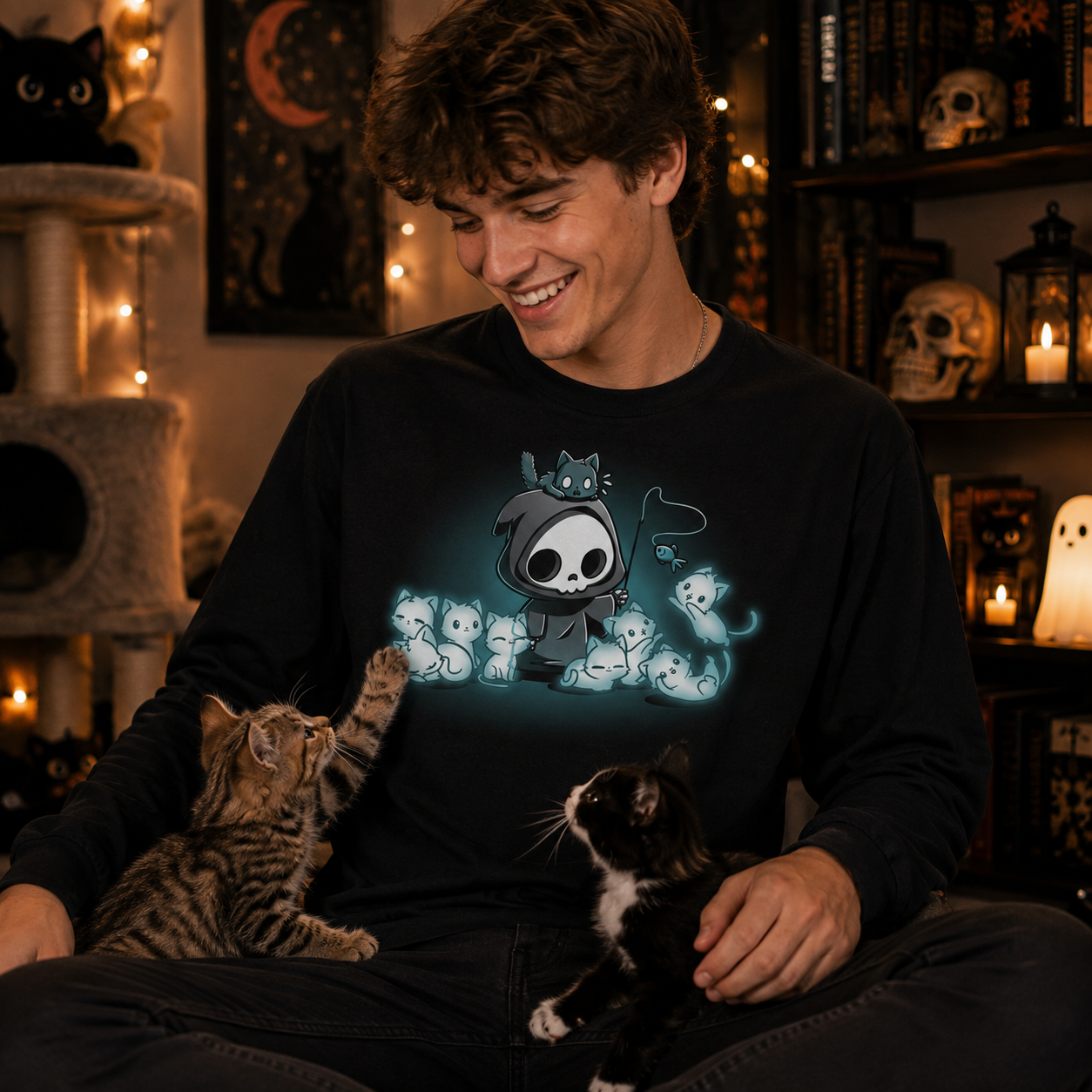 Long Sleeve T-shirt_TeeTurtle Grim and Kitties black t-shirt featuring a hooded skeleton figure, resembling a spooky Grim Reaper, standing surrounded by glowing ghostly cats. One cat is perched on its head while it playfully dangles a toy fish in front of the others.