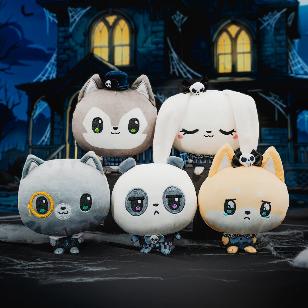 Five cute plush cat toys in different colors and outfits, arranged together in front of a spooky haunted house backdrop with cobwebs and glowing windows.
