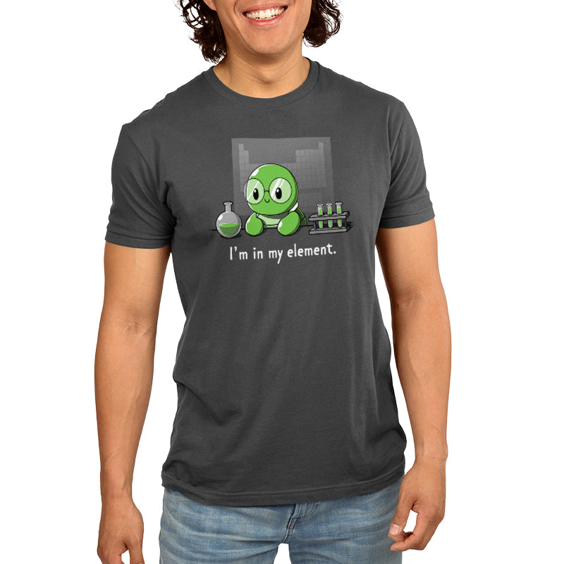 A person wearing a charcoal gray T-shirt with a cartoon of a green character in a lab setting and the text "I'm in My Element" by monsterdigital. The Super Soft Ringspun Cotton fabric adds extra comfort to their look.