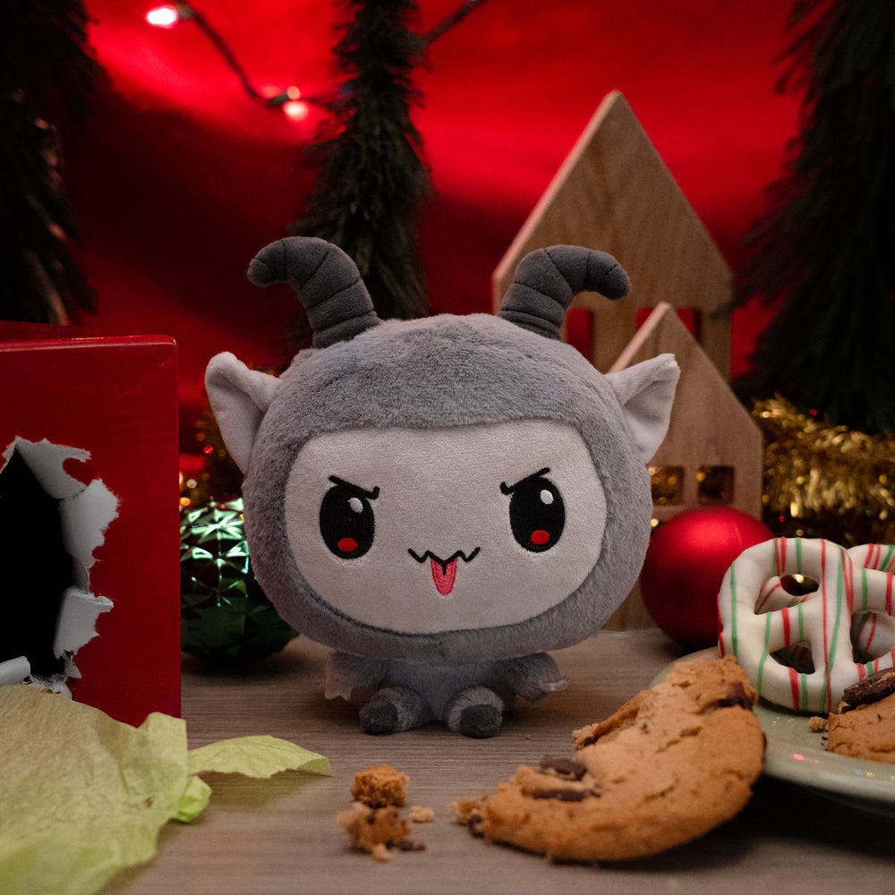 Cloudheads: 5" Krampus surrounded by holiday items, such as a torn-up present box, wrapping paper, chocolate chip cookies, pretzels, tree branches, Christmas lights and tree ornaments.