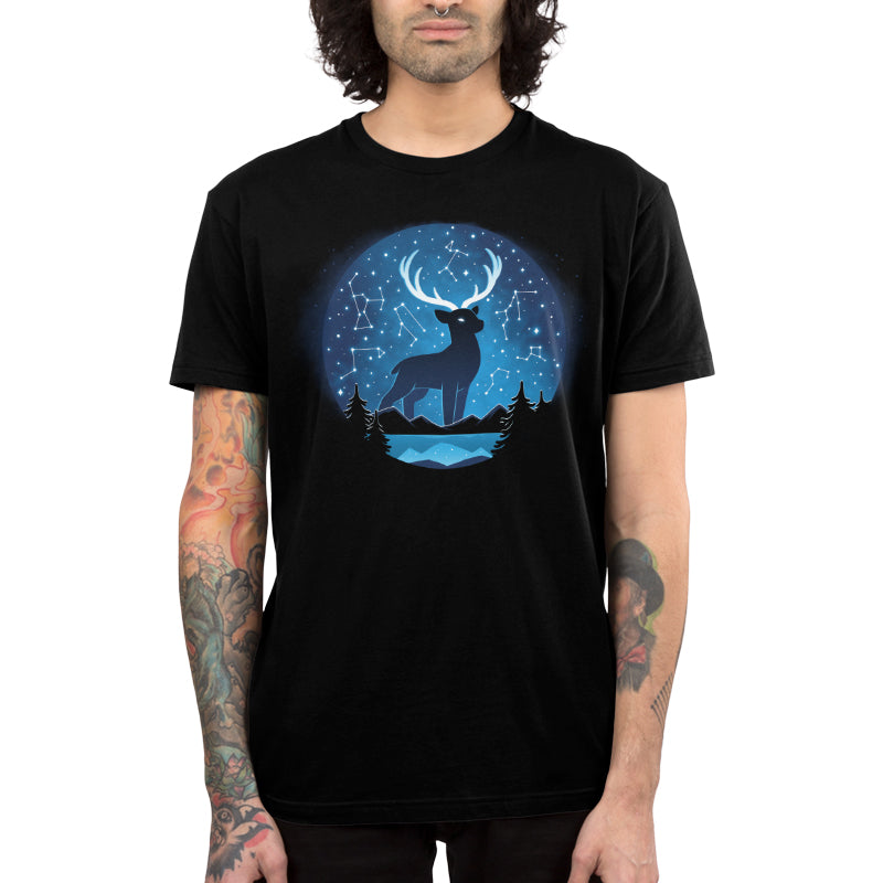 Premium Cotton T-shirt_TeeTurtle Celestial Stag (Glow) black t-shirt featuring a silhouette of a deer with large antlers in a circular frame against a backdrop of a starry night sky with constellation patterns. In the foreground, there are dark silhouettes of coniferous trees, light-blue horizontal lines representing mountains and a body of water. 