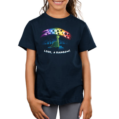 Premium Cotton T-shirt_TeeTurtle Look, a Rainbow! navy blue t-shirt featuring a green dinosaur looking up at rainbow asteroids in the starry night sky. The background is filled with black palm trees in the distance being illuminated from the asteroids, with "LOOK, A RAINBOW!" written underneath the illustration.