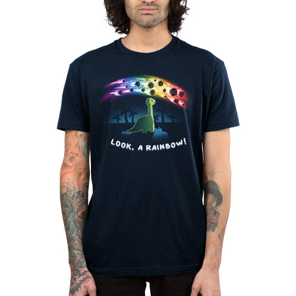 Premium Cotton T-shirt_TeeTurtle Look, a Rainbow! navy blue t-shirt featuring a green dinosaur looking up at rainbow asteroids in the starry night sky. The background is filled with black palm trees in the distance being illuminated from the asteroids, with "LOOK, A RAINBOW!" written underneath the illustration.