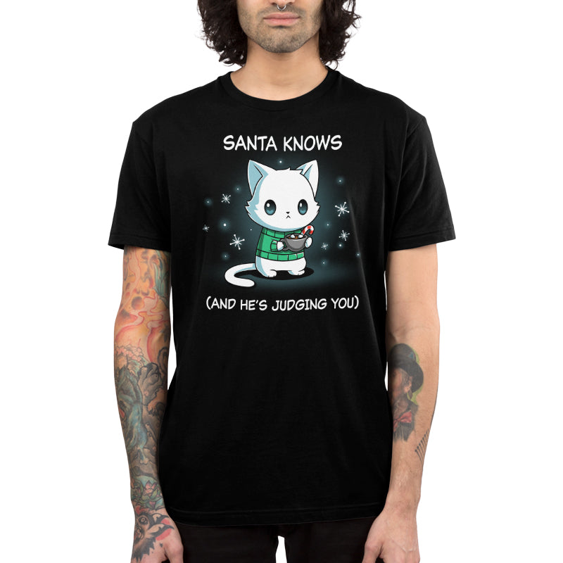 Premium Cotton T-shirt_TeeTurtle black Santa Knows apparel featuring a cat with a deadpan expression holding mug with hot chocolate, marshmallows, and a candy cane surrounded by snowflakes, with the caption, “Santa Knows (And He’s Judging You)“.