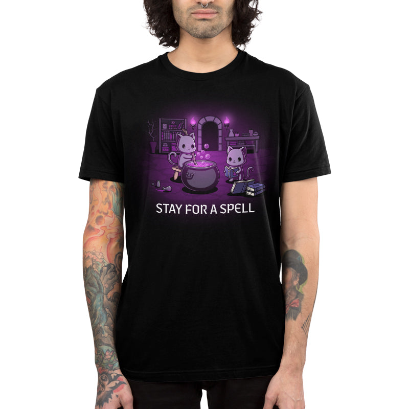 Premium Cotton T-shirt_TeeTurtle black Stay For A Spell apparel featuring two black cats in a spooky dungeon with one cat on a stool stirring a large cauldron, and the other cat reading from a pile of spellbooks with books, witchcraft accessories, and potion-making equipment in the background.