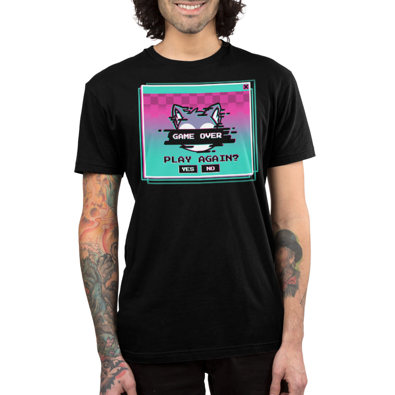 The person is wearing a unisex tee made from super soft ringspun cotton, featuring a colorful "Game Over" screen graphic with a cat and the text "Play Again? YES NO." Their tattooed arms add an extra touch of personality to the ensemble. The product name is Game Over, Play Again? by monsterdigital.
