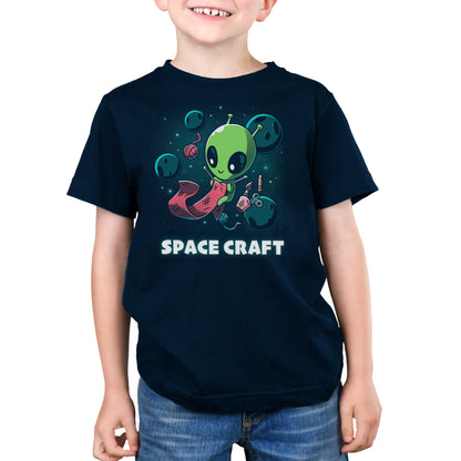 Premium Cotton T-shirt_TeeTurtle Space Craft navy blue t-shirt featuring an illustration of a green alien knitting a red scarf in space surrounded by planets, stars, balls of yarn, and a cup holding scissors, a paint brush and floating pencil. The words "SPACE CRAFT" are written below.