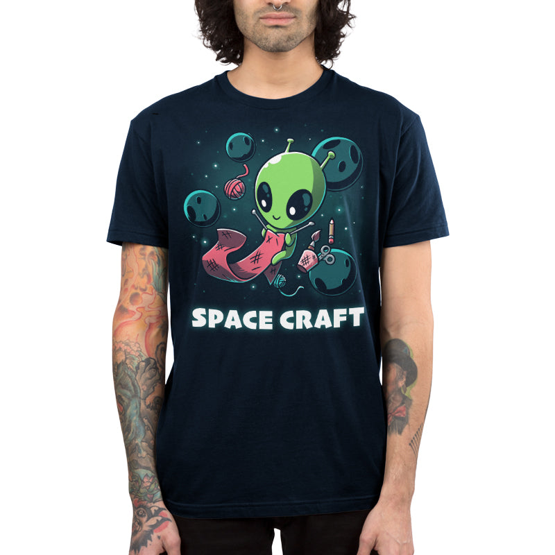 Premium Cotton T-shirt_TeeTurtle Space Craft navy blue t-shirt featuring an illustration of a green alien knitting a red scarf in space surrounded by planets, stars, balls of yarn, and a cup holding scissors, a paint brush and floating pencil. The words "SPACE CRAFT" are written below.