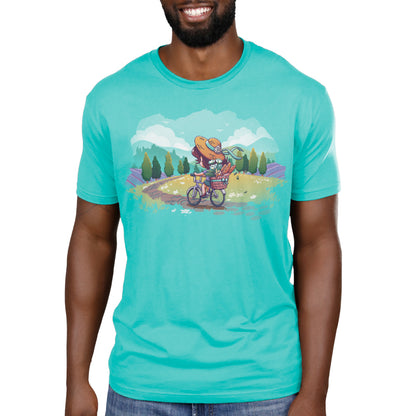 Premium Cotton T-shirt_TeeTurtle Countryside Biking Caribbean blue t-shirt featuring an illustration of a girl biking on a path in the countryside with bread and flowers in her basket. The path winds through rolling hills and fields of grass with small, white flowers. Green trees line the sides of the path, and lavender bushes are behind the trees, set against a light teal/turquoise sky, with fluffy white clouds and some birds.