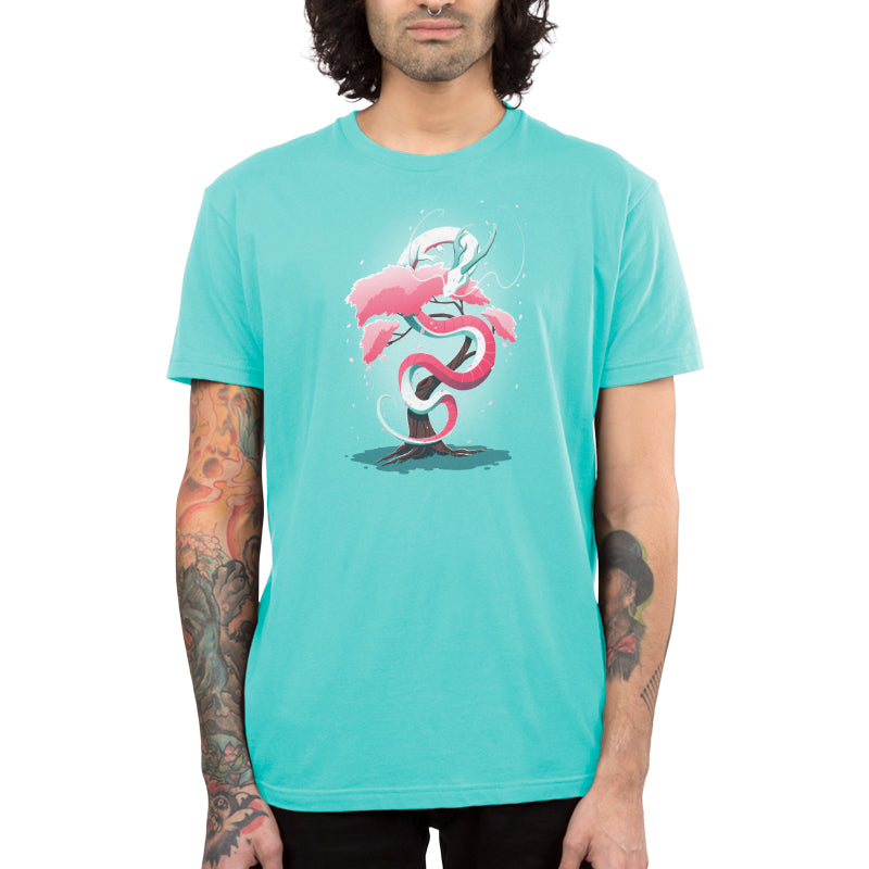 Person wearing a monsterdigital Cherry Blossom Dragon T-shirt with a stylized design of a coiled snake and tree. They have tattoos on both forearms and dark, curly hair hanging loose.