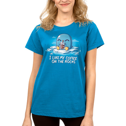 A person wearing a cobalt blue t-shirt featuring a cartoon penguin holding iced coffee and the text "I like my coffee on the rocks." The I Like My Coffee on the Rocks t-shirt by monsterdigital is made from super soft ringspun cotton for ultimate comfort.