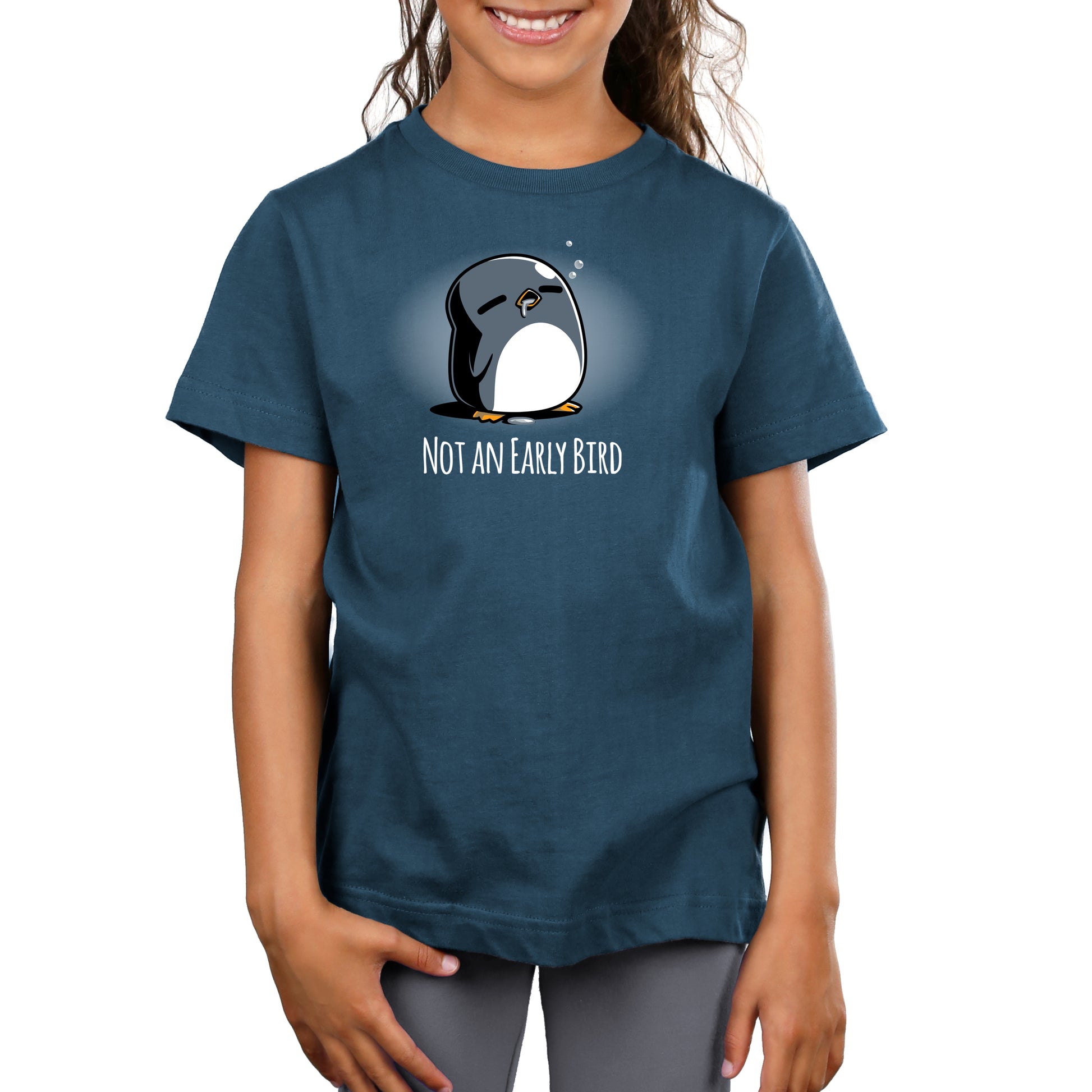 A smiling child wears a Not an Early Bird t-shirt by monsterdigital, made from super soft ringspun cotton, adorned with a sleepy cartoon penguin and the text "Not an Early Bird.