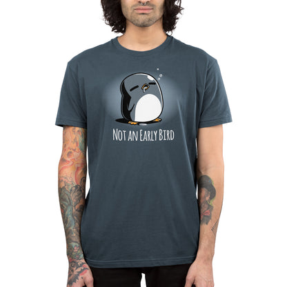 A person wearing a super soft ringspun cotton T-shirt by monsterdigital with a penguin illustration and the text "Not an Early Bird" stands against a neutral background, with visible tattoos on their arms.