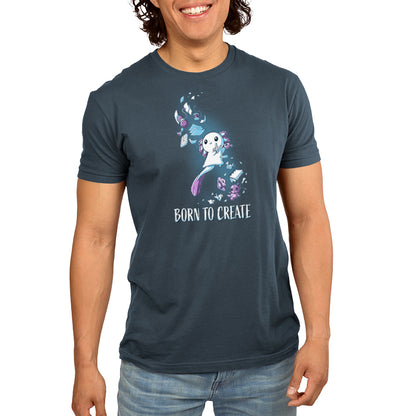 Person wearing a denim blue T-shirt with a whimsical design of a creature surrounded by flowers and leaves, made of super soft ringspun cotton, with the phrase "Born to Create" printed below the design. The T-shirt is the Born to Create from monsterdigital.