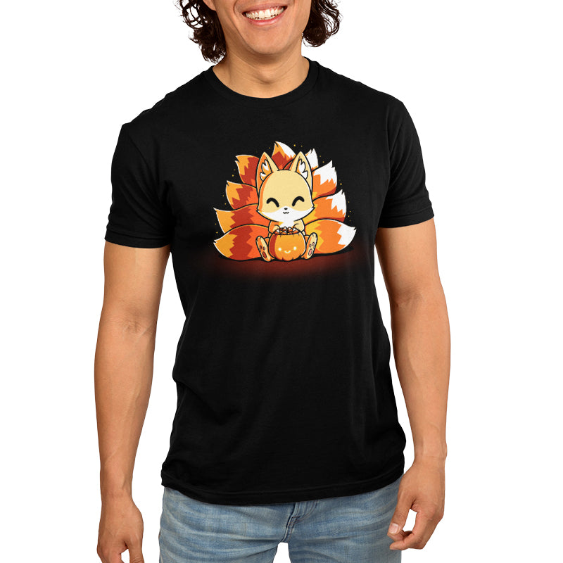 Person wearing a super soft ringspun cotton black monsterdigital original T-shirt featuring a cute, Candy Corn Kitsune with multiple tails, sitting and holding a pumpkin.