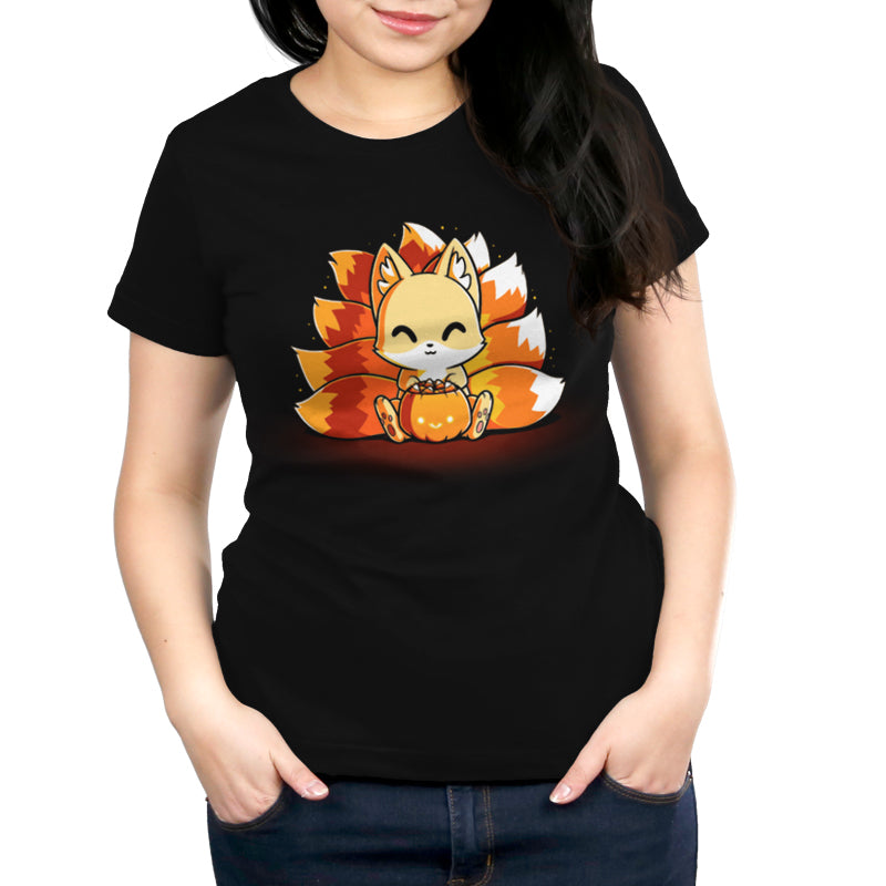 A person wearing a black T-shirt with an illustration of a cute Candy Corn Kitsune sitting and holding a pumpkin, from monsterdigital original.