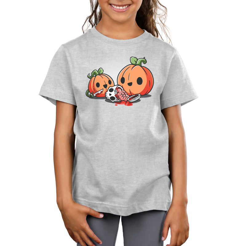 A girl is wearing a light grey monsterdigital Pumpkin Carving t-shirt with a cartoon image of two jack-o'-lanterns and a soccer ball. One jack-o'-lantern is spilling its guts, with seeds and stringy pulp visible, all on super soft ringspun cotton.
